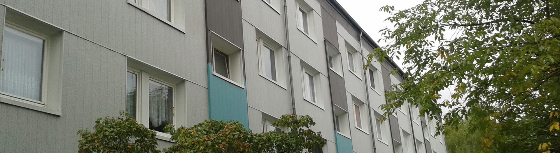 Ein Ausschnitt eines Wohnhauses von außen mit vielen Fenstern und türkisfarbenen Akzenten an der Hauswand